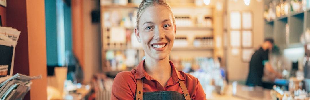 Business owner of coffee shop standing in front of counter and smiling with arms crossed
